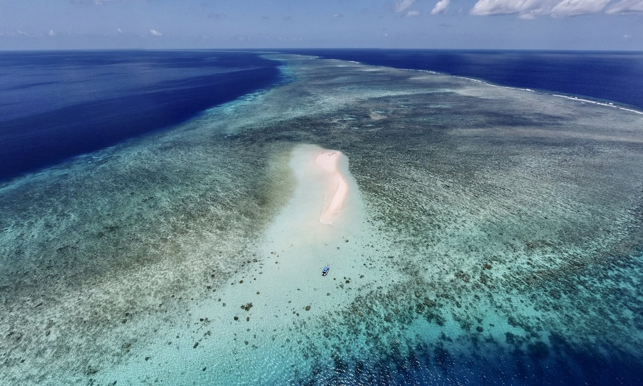 Vue aérienne du lagon de Mayotte : un îlot de sable posé sur la barrière de corail, un bateau au mouillage