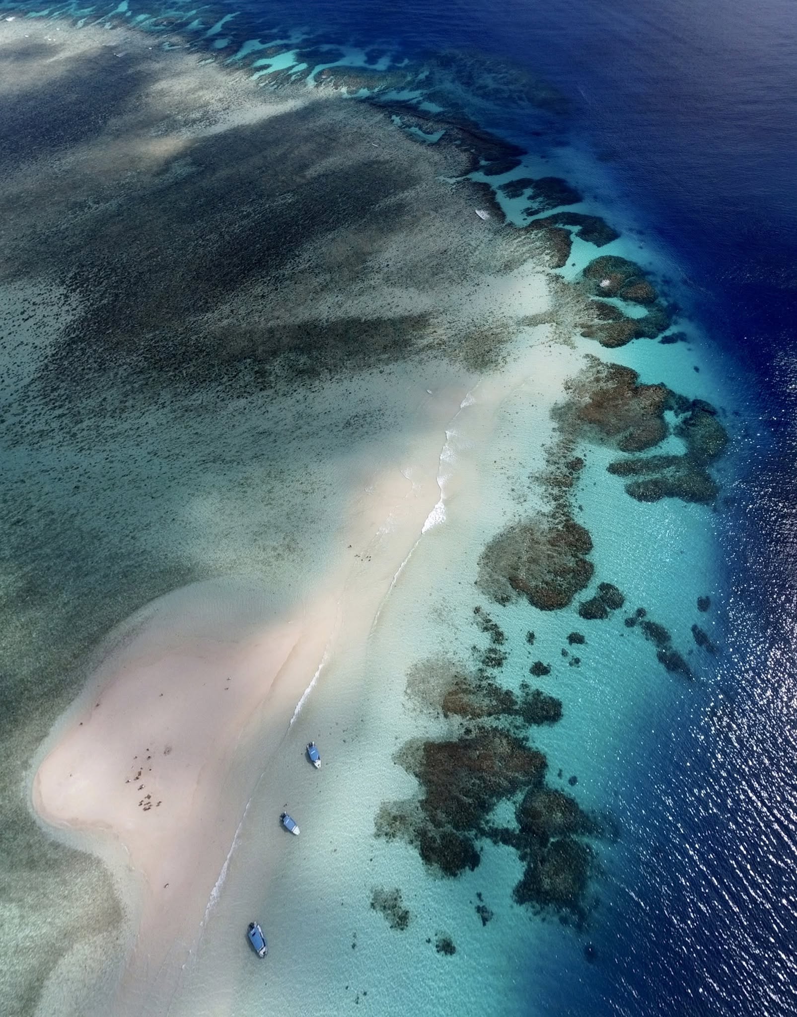 Banc de sable du lagon de Mayotte vu du ciel, trois bateaux au mouillage le long du récif